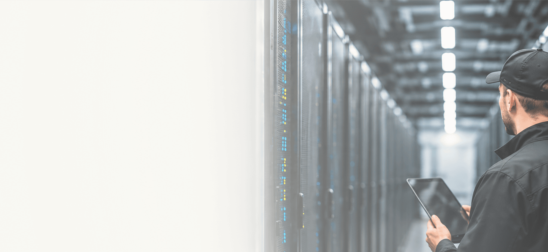 Technician holding a tablet and looking down an aisle of server racks in a data center